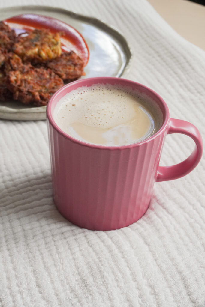 Chai Masala Latte in a pink cup with a plate of Pakoras with sauce on the side on a beige grey plate in the background