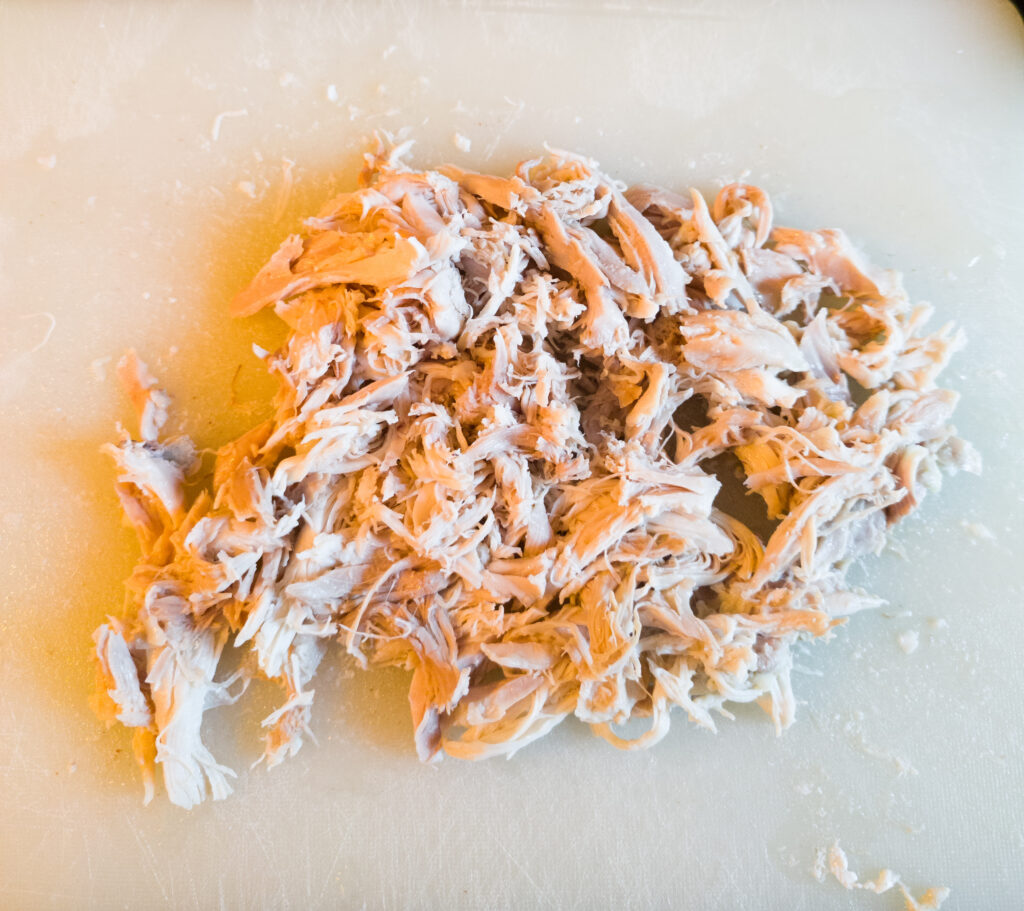 Shredded chicken meat on a white cutting board