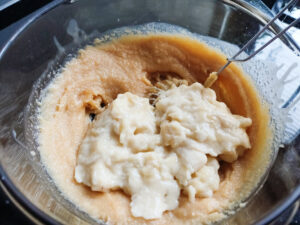 Adding mashed bananas into the cake batter in a bowl