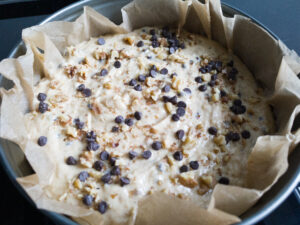 Roasted walnuts and chocolate chips evenly distributed on cake batter in a baking pan