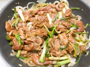 Adding beef mrinade mixture with the sauteed onions in a pan