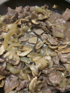 Adding beef stock cube to beef stroganoff in a pan