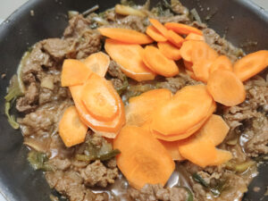 Adding carrots into stir fry beef in a pan