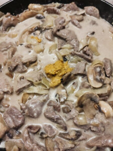 Adding dijon mustard to beef stroganoff in a pan