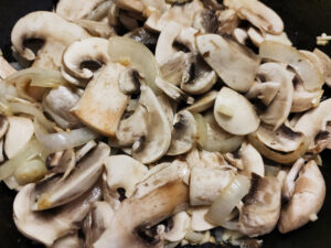 Adding mushrooms to sauteed onions and garlic in a pan