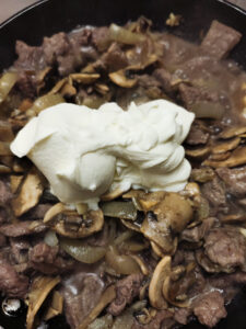 Adding crème fraîche to beef, mushrooms, garlic and onions