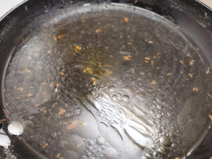 Adding water to ghee and jeera in a pan