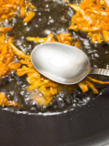 Flattening pakoras with a spoon while frying in a pan