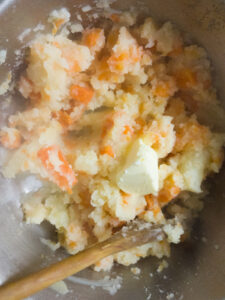 Adding butter to roughly mashed vegetables in a bowl