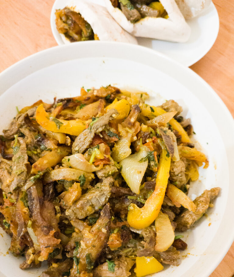 Lomo Saltado in big bowl with pita breds stuffed with lomo saltado in the background