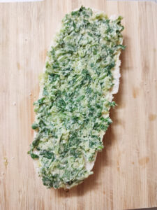 Spreading cilantro garlic butter mix on halved mini baguette on a cutting board