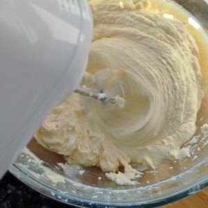 Incorporating mascarpone cheese into the cake batter in a bowl using the hand mixer