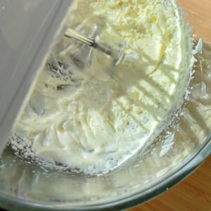 Process of whisking heavy cream and sugar together in a bowl using a hand mixer