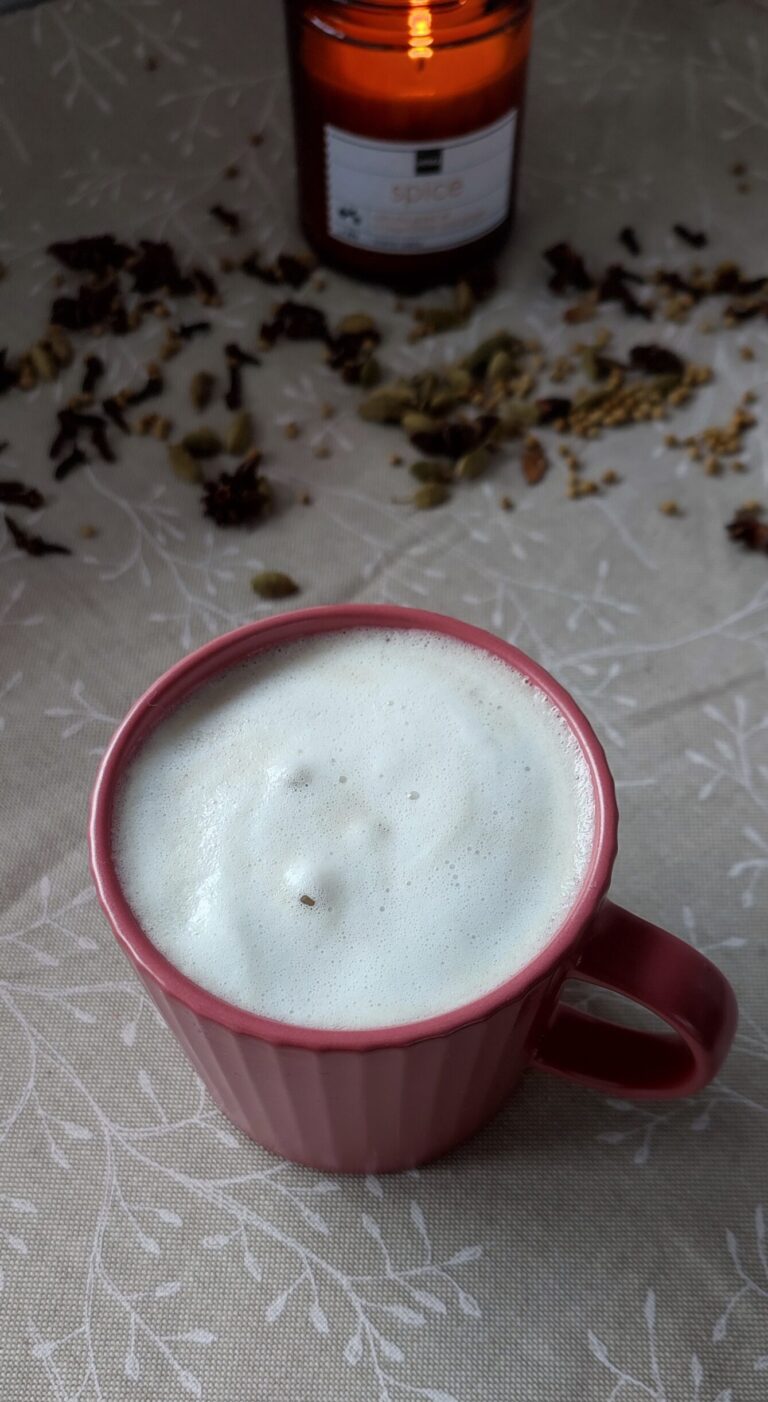 Masala Chai Latte accompanied by trail of spices and a candle light in the background