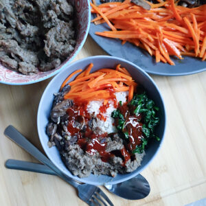 Assembly of rice, vegetables, bulgogi and gochujang sauce mix with stir fried carrots and bulgogi in the background