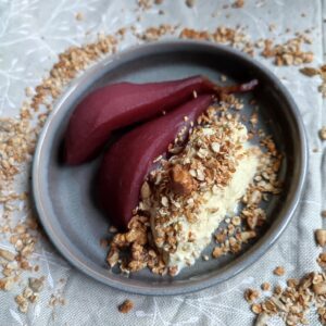 Stoofpeertjes to serve : Two pieces of pear with a scoop of ice cream and a sprinkle of granola on a dessert plate surrounded by a ring of granola trail