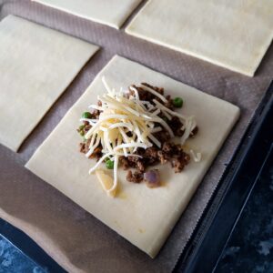 Add cheese on top of the beef keema on the pastry square sheet on a lined baking tray