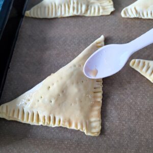 Egg wash on Cheesy Keema Puff before baking on a lined baking tray