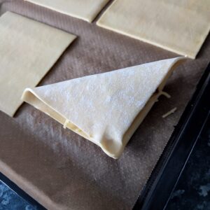 Fold the above corner to the bottom corner diagonally and pinch the end of the puff pastry on the baking tray