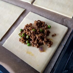 Place a small portion of beef keema in each puff pastry square sheet on a lined baking tray