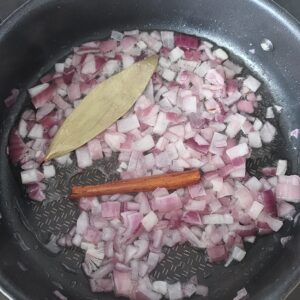 Sautéed chopped onions, bay leaf and cinnamon stick in a pan