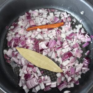 Sautéing chopped onions, bay leaf and cinnamon stick in a pan