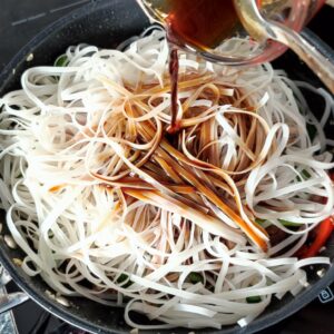 Adding drained soaked flat rice noodles and stir fry sauce in a wok