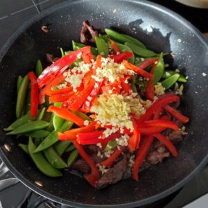 Adding sugar snap peas, thinly sliced bell pepper, minced garlic and minced ginger in a wok