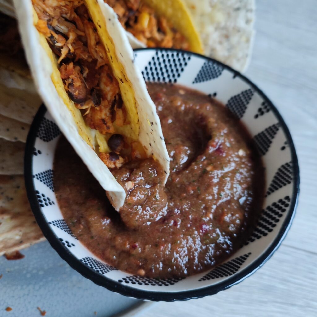 B roll 1 Crunchy Chicken Tacos : dipping crunchy chicken taco into a black and white patterned bowl of pureed pico de gallo with a few crunchy chicken tacos on a grey plate in the background