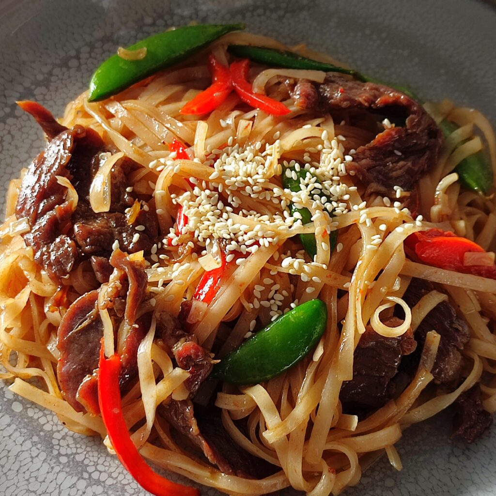 B roll 2 Stir fry beef noodles garnished with roasted sesame seeds on a large gray plate