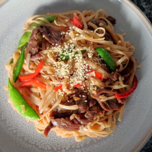 Stir fry beef noodles garnished with roasted sesame seeds on a large gray plate ready to be served