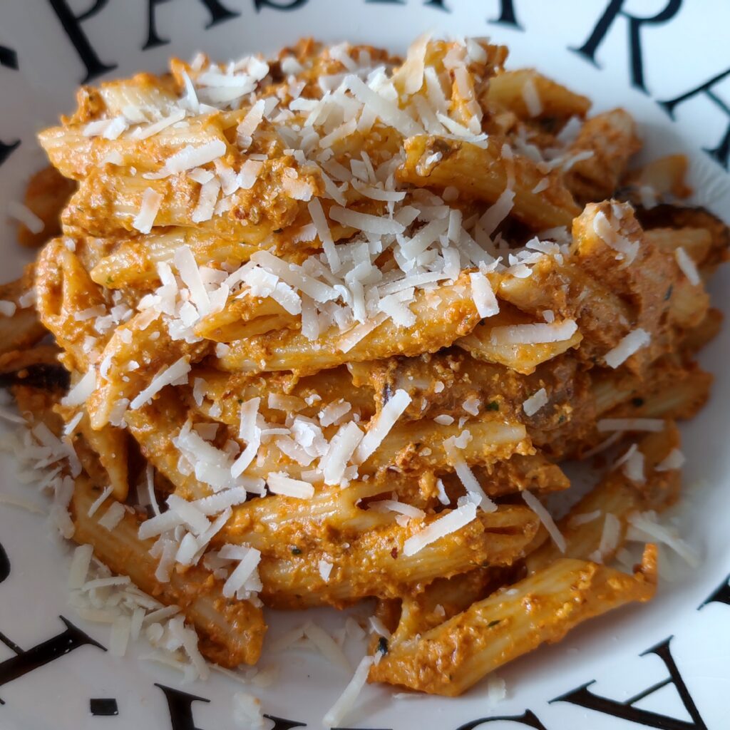 B Roll 1 Pasta Pesto Rosso with Shiitake Mushrooms garnished with Parmigiano Reggiano on a white plate with black lettering