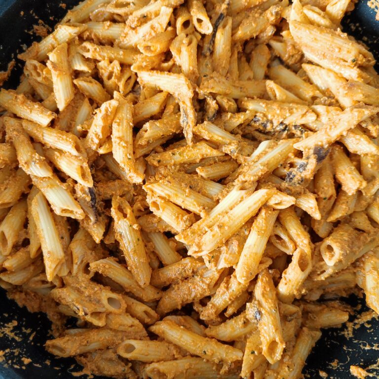 Mixing in the cooked penne with red pesto and shiitake mushrooms in the pan on the stove