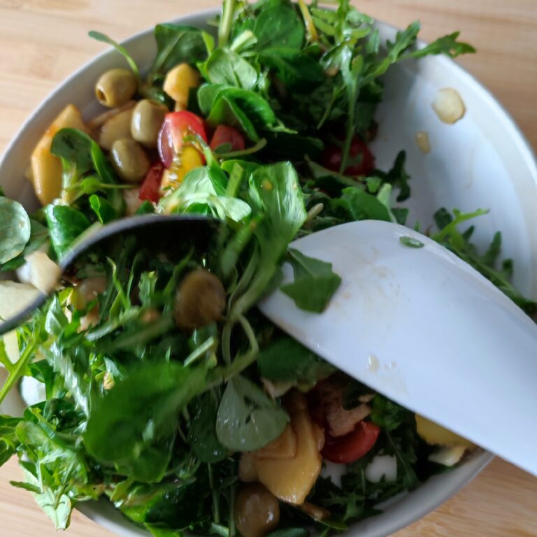 Mixing the salad and vinaigrette together with one spatula and a spoon in a large bowl on the working surface