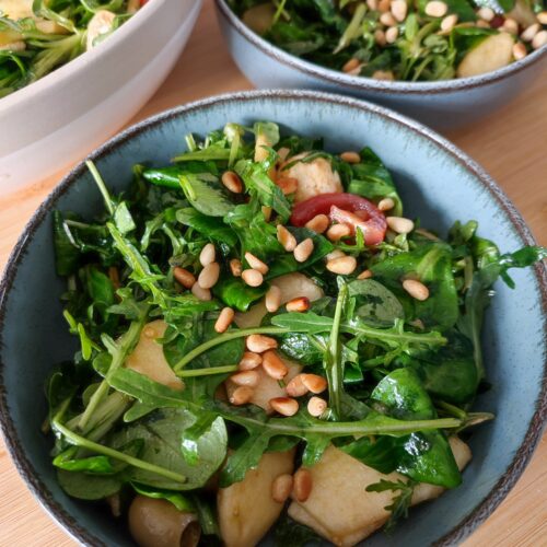 The Everything Salad portioned between two blue bowls with the large bowl of leftover salad in the background on a working surface