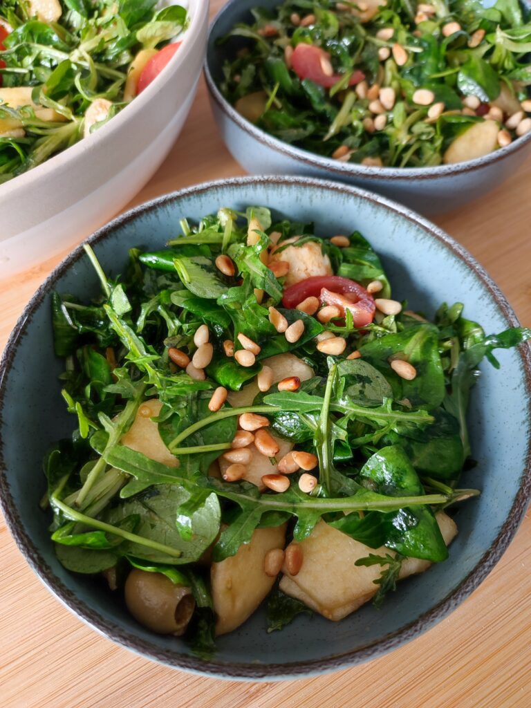 The Everything Salad portioned between two blue bowls with the large bowl of leftover salad in the background on a working surface