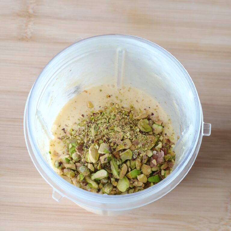 Adding roasted crushed pistachios in to the blended ingredients in a smoothie blender on the working surface