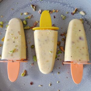 Mango Cardamom Pistachio Popsicles topped with roasted pistachios on a large gray plate