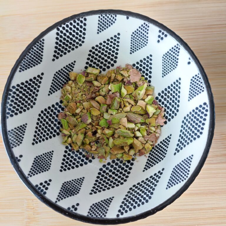 Roughly crushed roasted pistachios in a black and white patterned bowl on a working surface