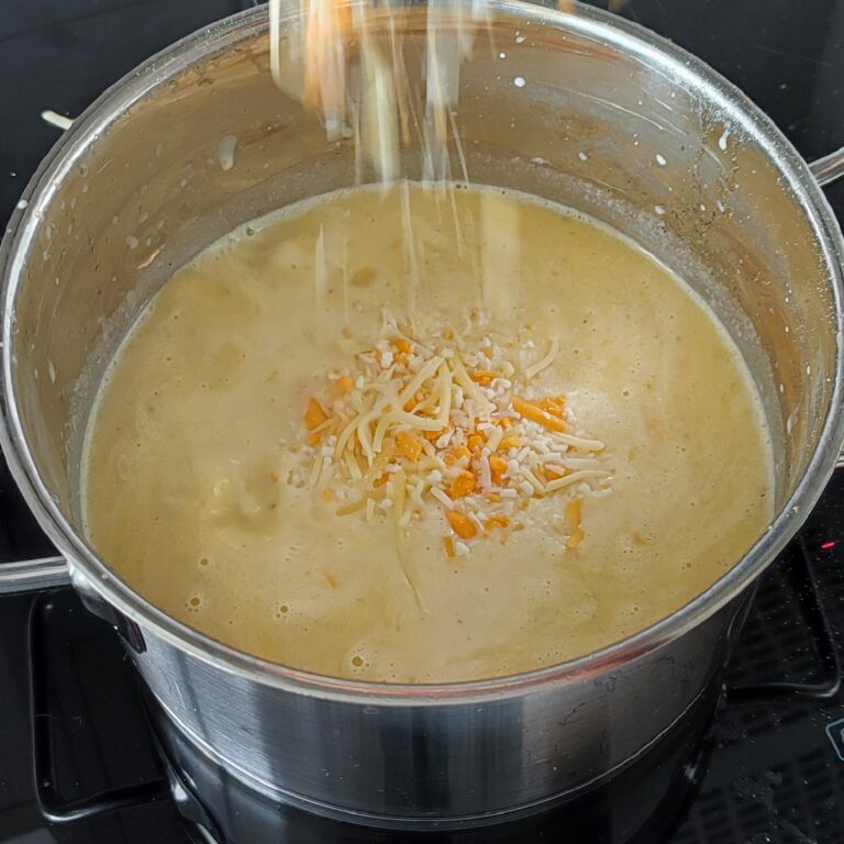 Adding the shredded cheeses in to the creamy mixture in the pot