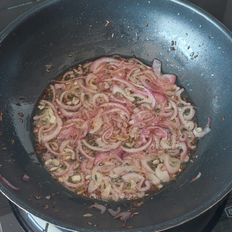 Adding sliced red onions to sauté in a large pan