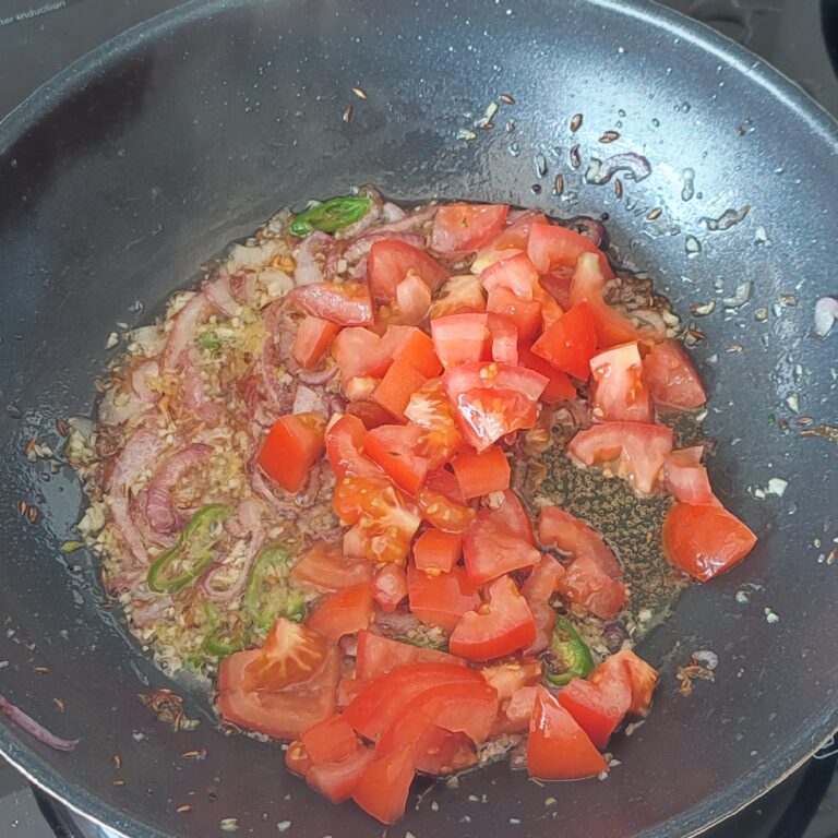 Adding chopped tomatoes to sauté in a large pan