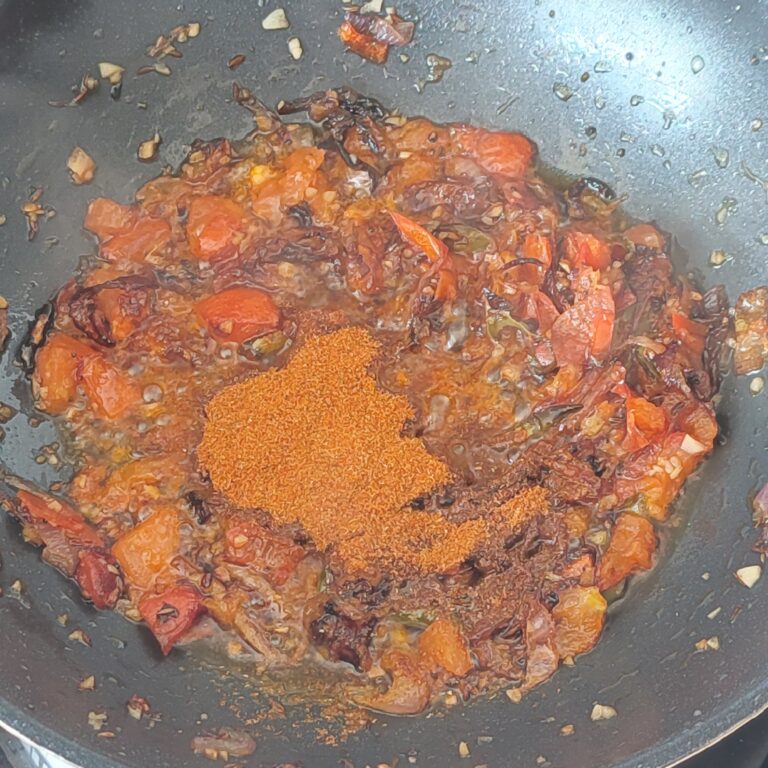 Adding spice mix with cooked down tomatoes in a pan