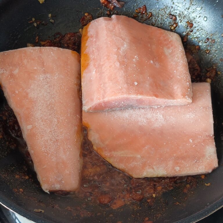 Adding frozen salmon fish fillets to tomato spice mixture