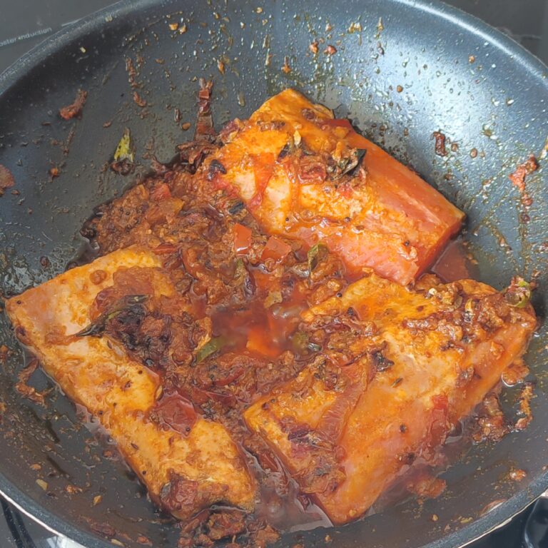 Letting fish fillets and tomato spice mixture cook in a large pan