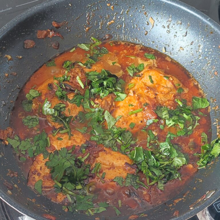 Adding fresh coriander to fish curry in a large pan