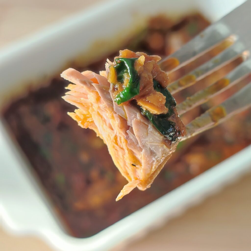 B roll 1 : South Indian Fish Curry piece on a fork with the rest of the fish curry in a casserole dish in the blurred background