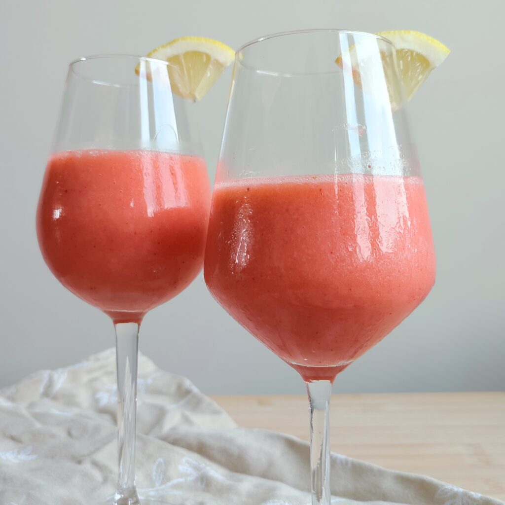 B roll 1: Pink Sgropinno in two wine glasses with a wedge of quartered lemon on the rims standing on taupe coloured fabric on a working surface close up shot