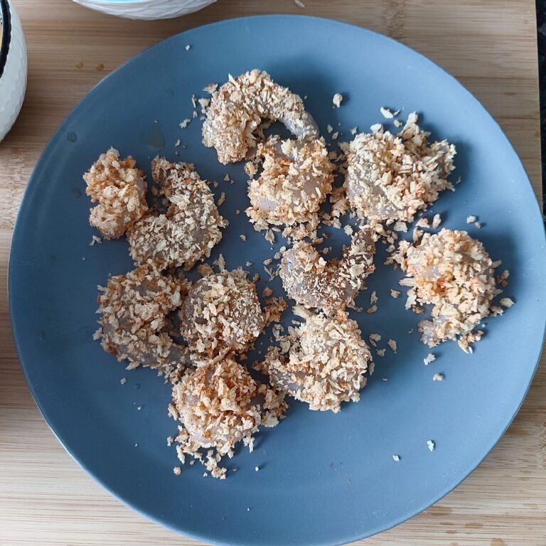 First batch of coated shrimps on a blue plate on a working surface