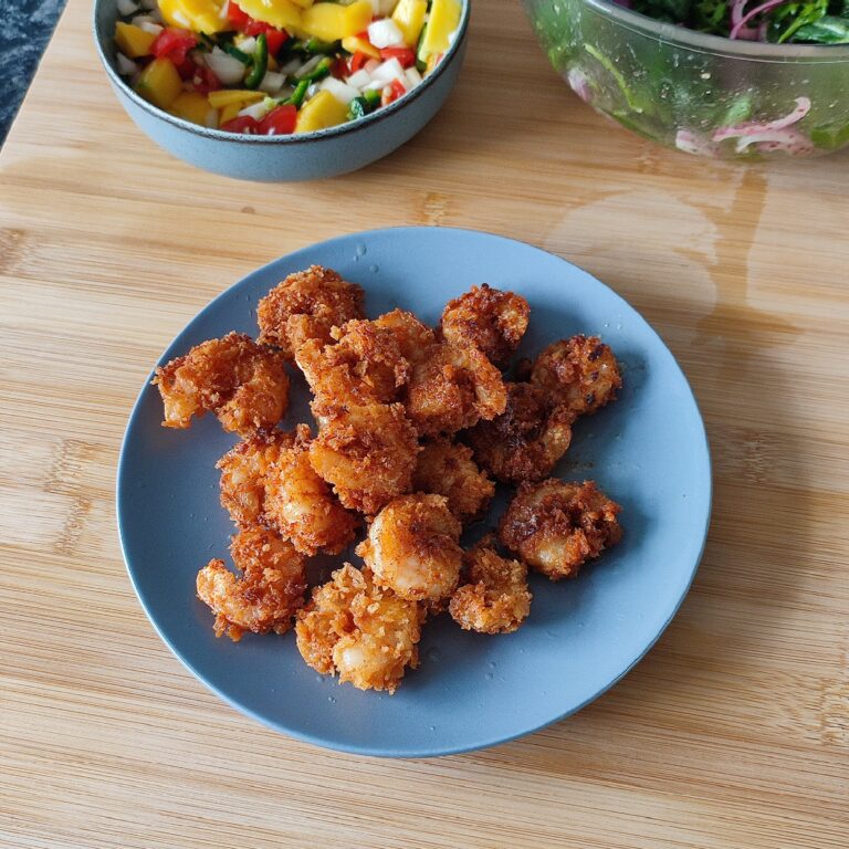 Fried Crispy Shrimp on a blue plate and the spicy mango salsa in a shallow blue bowl with the apple arugula sumac salad in the background and all on the working surface